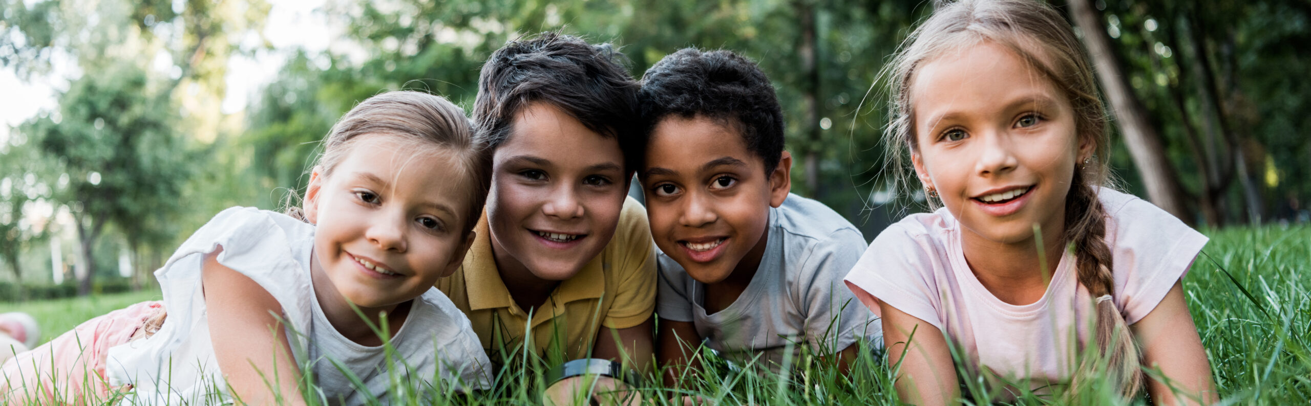 panoramic shot of cute multicultural children lying on grass